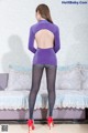 A woman in a purple top and black tights standing on a couch.