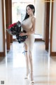 A woman in a beige dress holding a bunch of flowers.