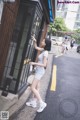 A woman standing in front of a phone booth on the street.