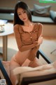 A woman in a brown shirt and stockings sitting on a chair.