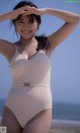 A woman in a white one piece swimsuit on the beach.