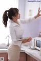 A woman in a white shirt and skirt standing in a kitchen.