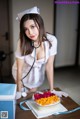 A woman in a nurse outfit with a cake on a table.