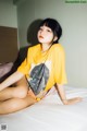 A woman sitting on a bed wearing a yellow shirt.