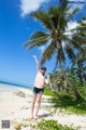 A woman standing on a beach next to a palm tree.