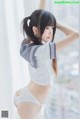 A woman in a white shirt and white panties posing by a window.